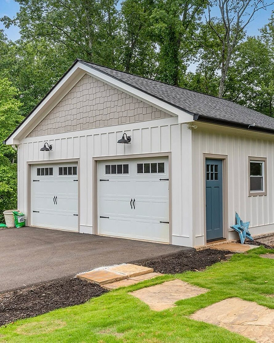 A white two-car garage with two garage doors, a blue side door, and a dark roof.