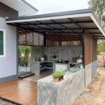 Modern concrete outdoor kitchen with a sink and stovetop under a covered porch structure.