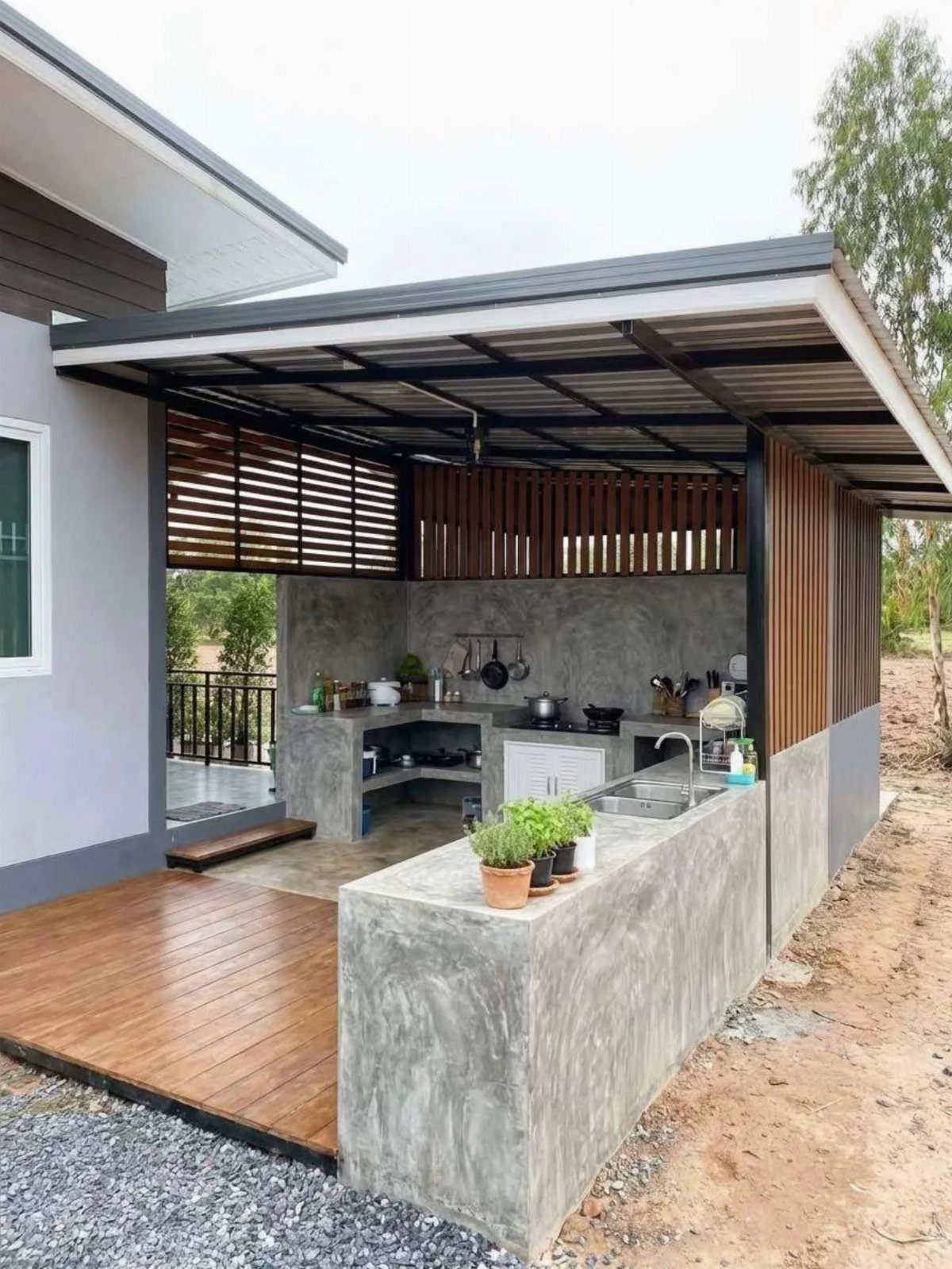 Modern concrete outdoor kitchen with a sink and stovetop under a covered porch structure.
