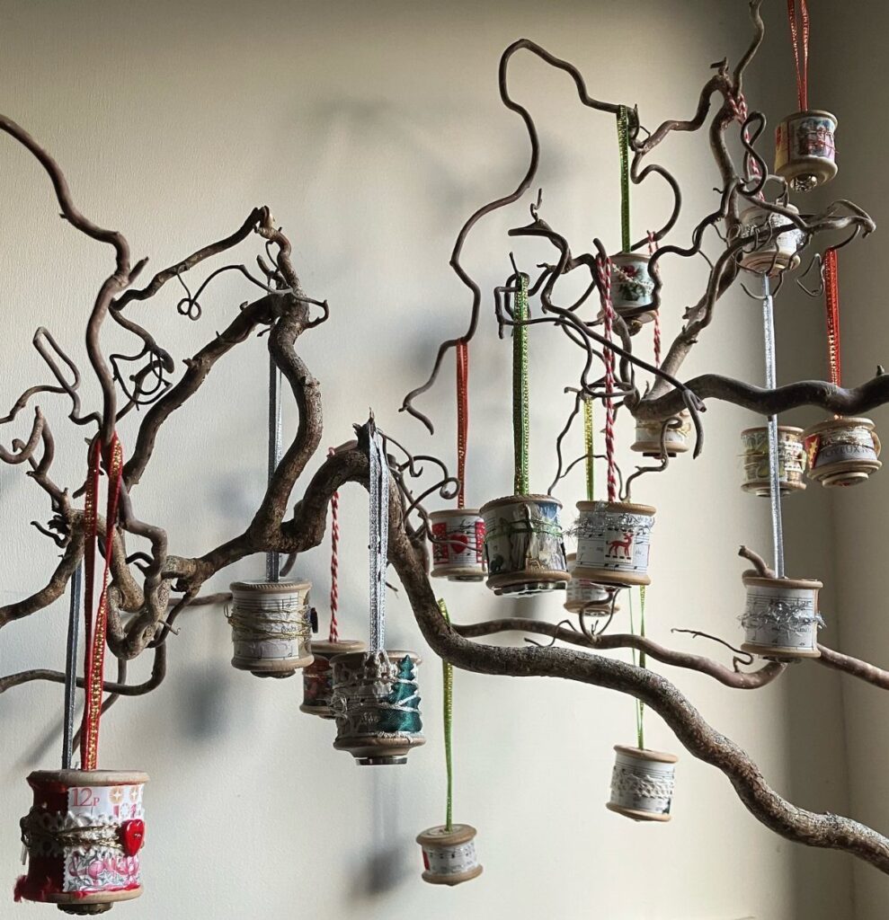 Decorated vintage wooden thread spools hanging from the branches of a large decorative wooden branch.