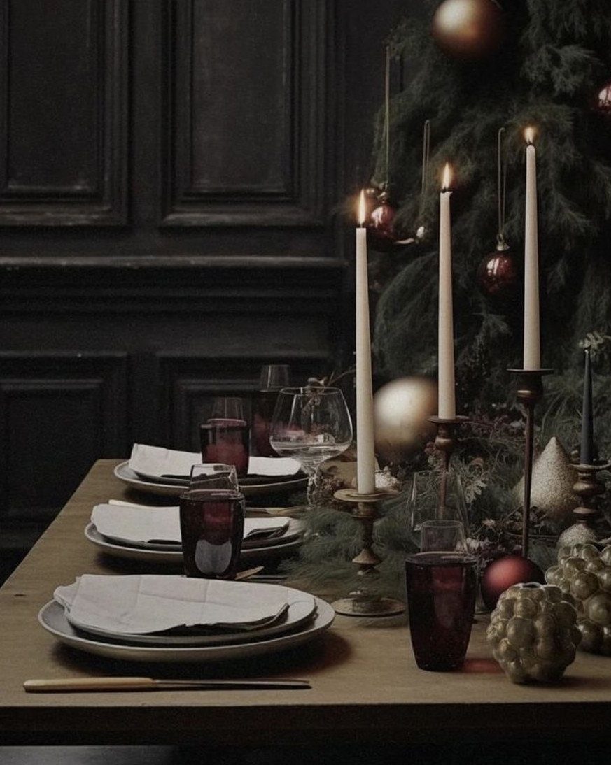 A festive dining table set with white plates, red glasses, and lit taper candles.
