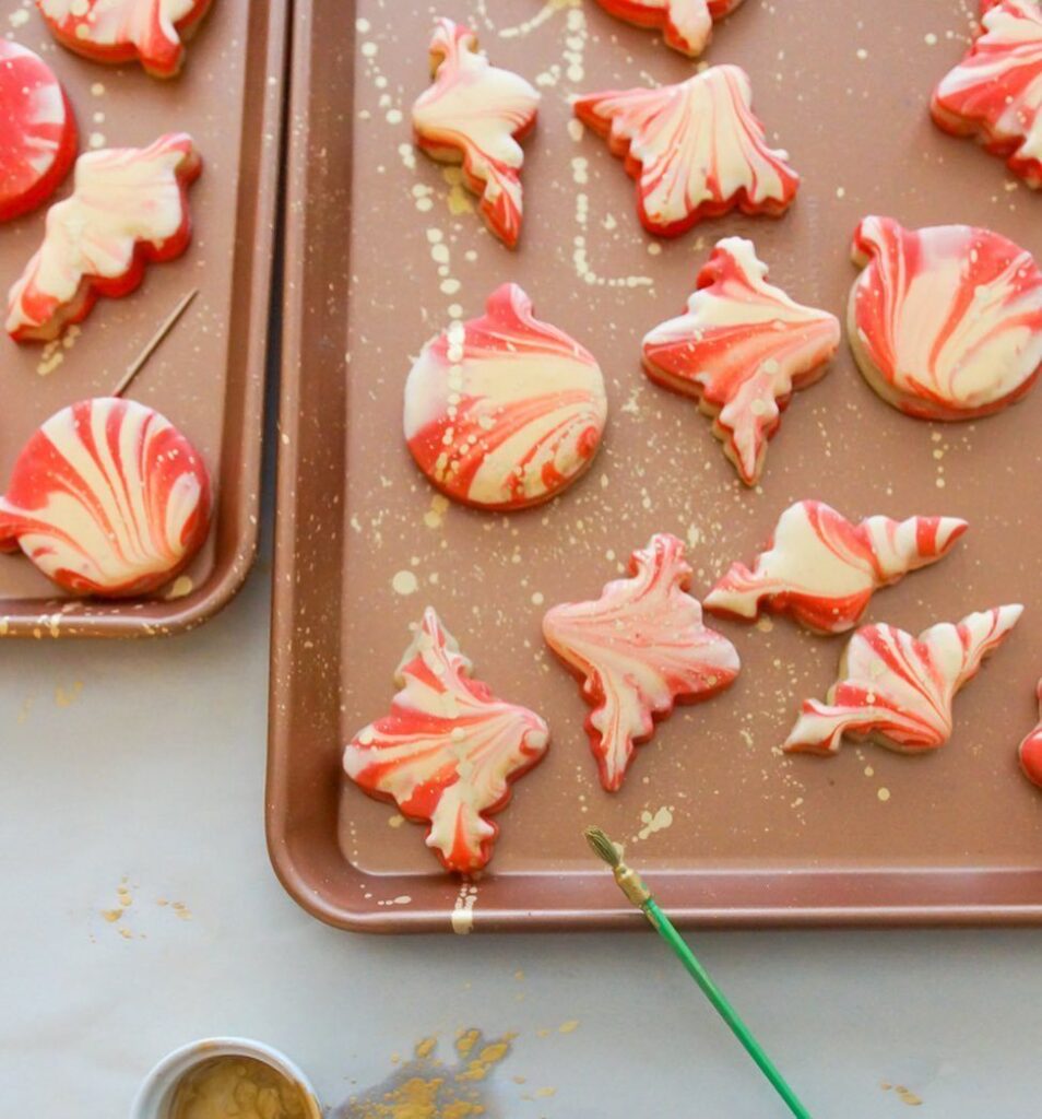 Red and white marbled icing decorated sugar cookies on brown baking sheets.