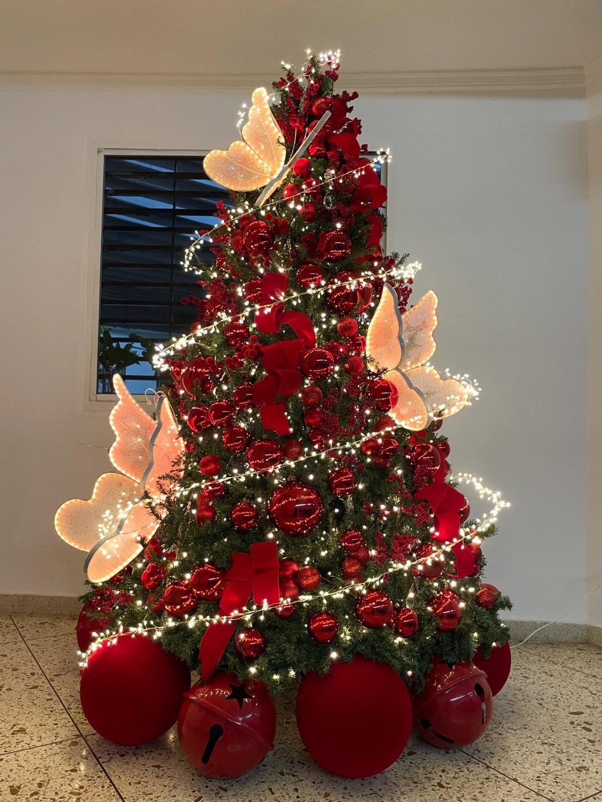 A decorated Christmas tree with red ornaments, white lights, and large butterfly decorations.