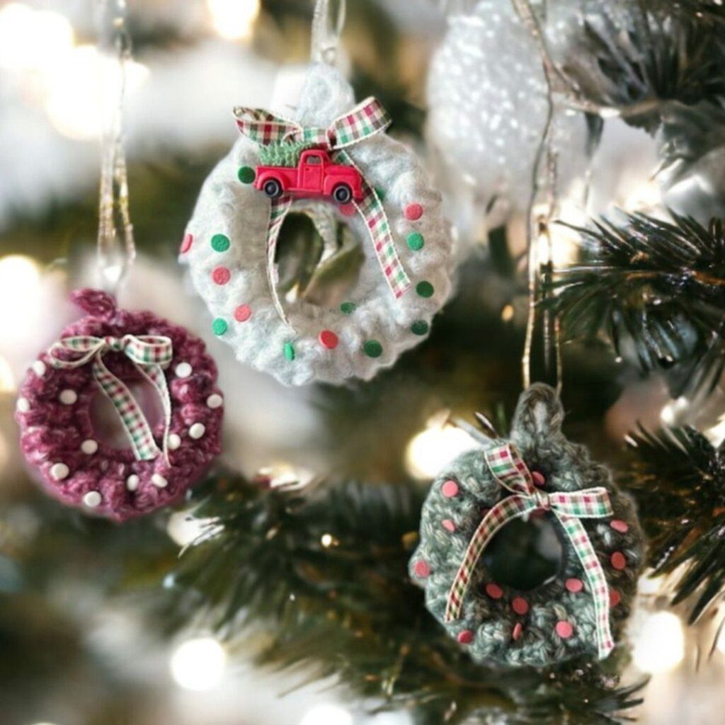 Three crocheted wreath ornaments with tiny bows hanging on a decorated Christmas tree.