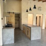 Concrete kitchen island with wooden cabinets under exposed wooden ceiling beams in a modern room.