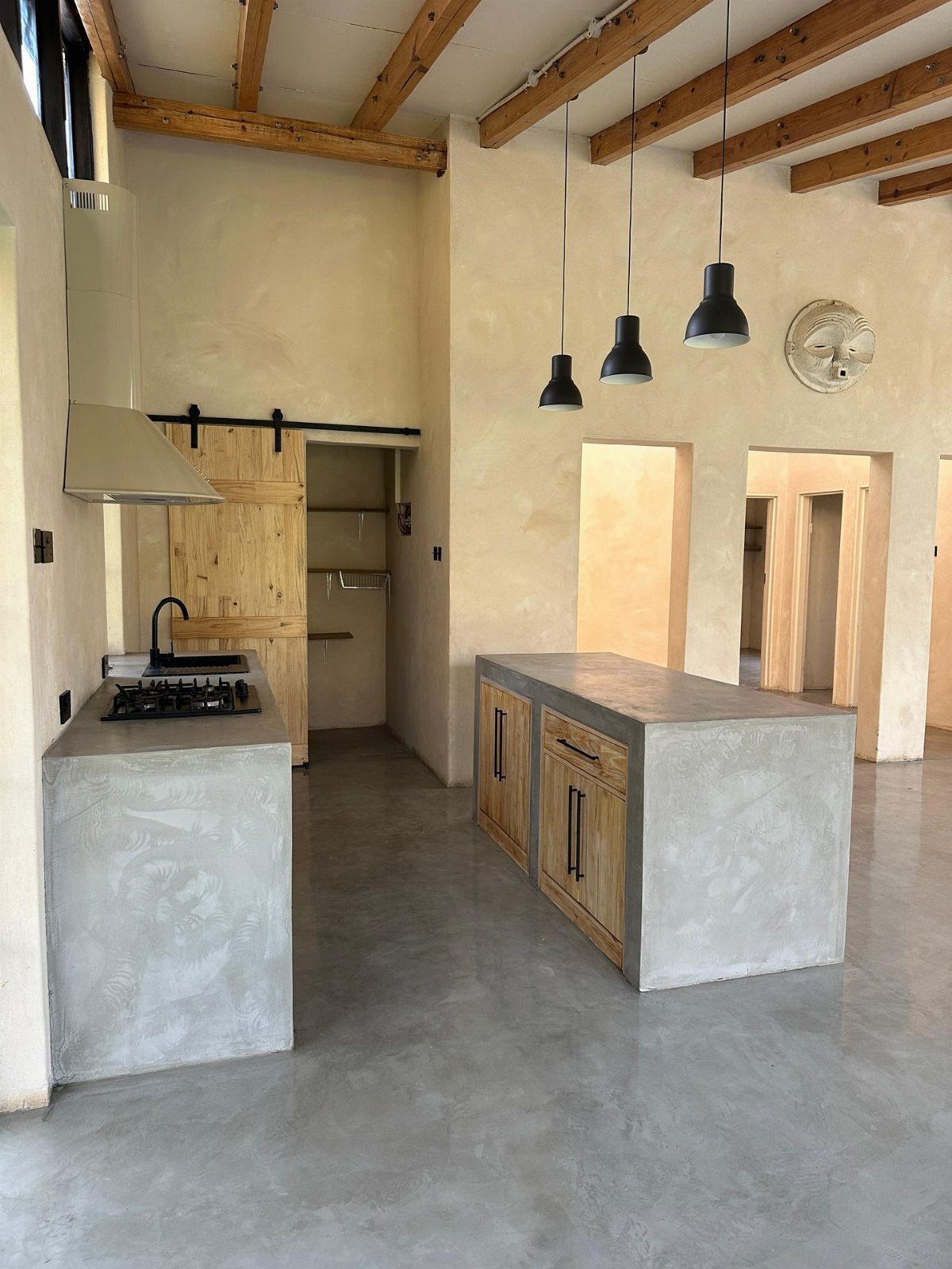 Concrete kitchen island with wooden cabinets under exposed wooden ceiling beams in a modern room.