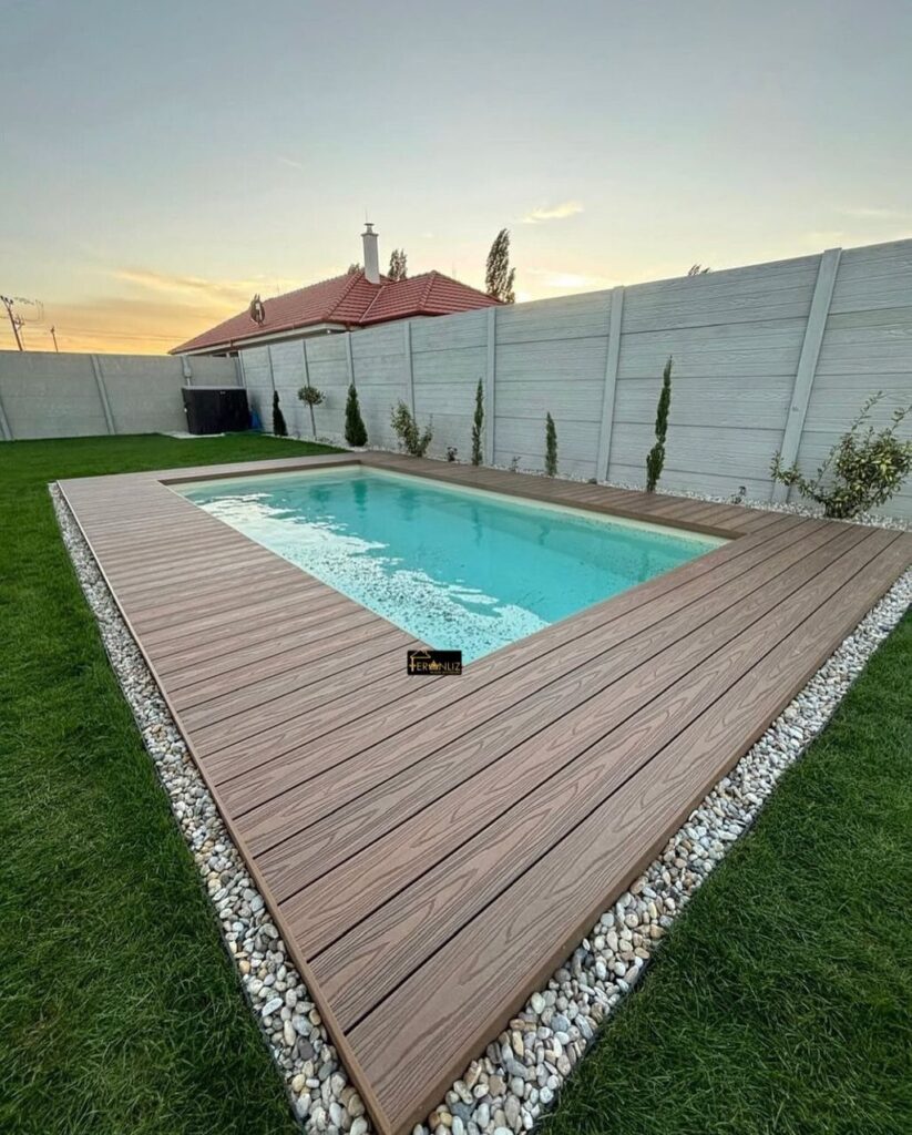 Brown wooden deck planks surrounding a bright blue swimming pool in a backyard garden.