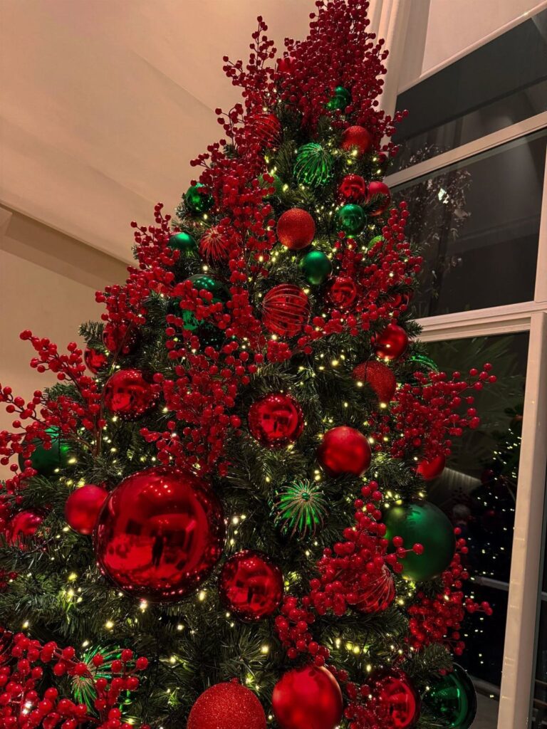Decorated Christmas tree with red berries, red and green ornaments, and glowing warm lights.